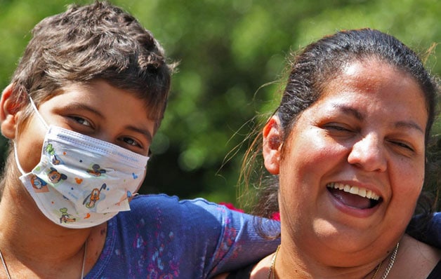 Two people smiling one with a face mask on