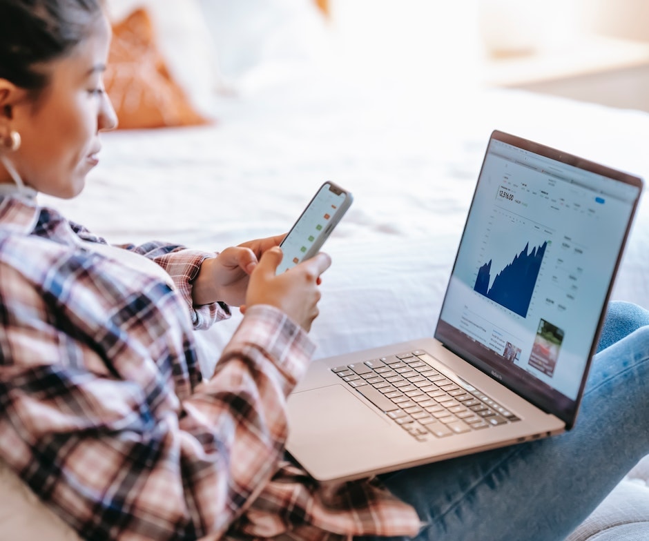 Person holding her phone while sitting on sofa and laptop with graph on the screen