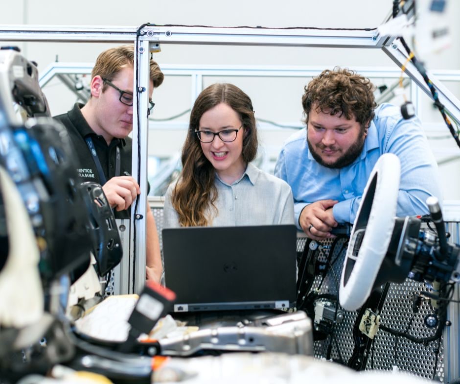 Three people working in a factory with a laptop