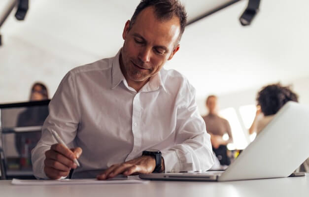 a man writing in front of laptop