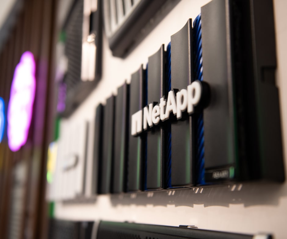 Close-up of a NetApp storage device mounted on a wall with other hardware components in the background