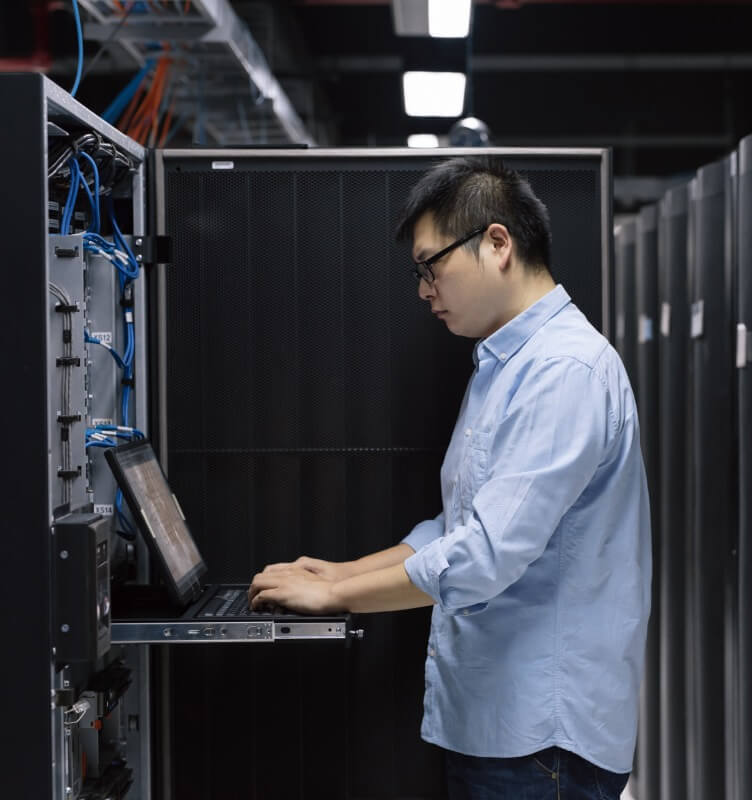 A man with a laptop in a darkened data center