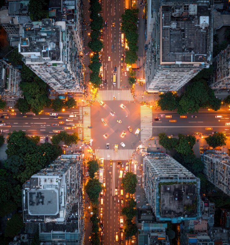 Aerial city intersection at night with illuminated buildings and traffic.