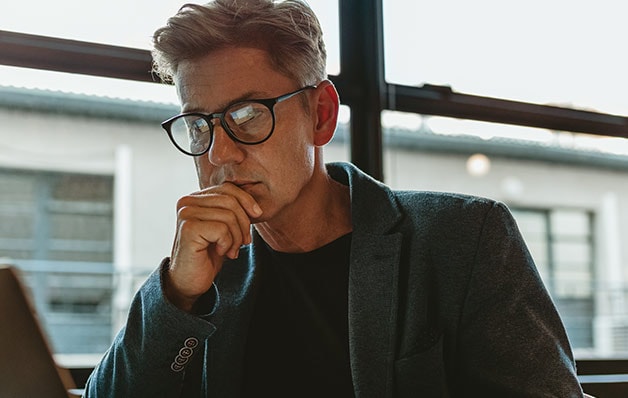 Un homme avec des lunettes noires regarde son ordinateur portable d'un air pensif