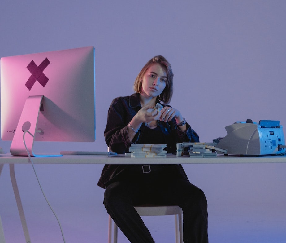 women sitting on desk with fax machine, iMac and cash on top of the table