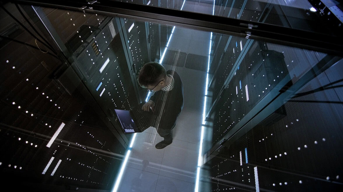 IT specialist working in a data center aisle surrounded by illuminated server racks.