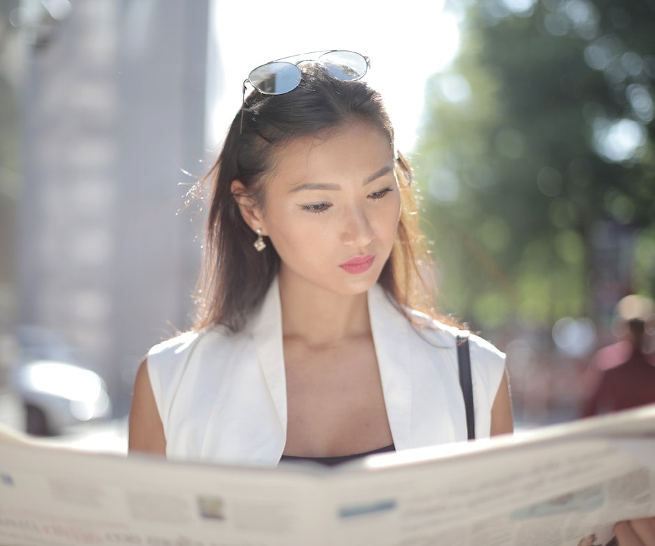 person reading newspaper while walking in sunshine