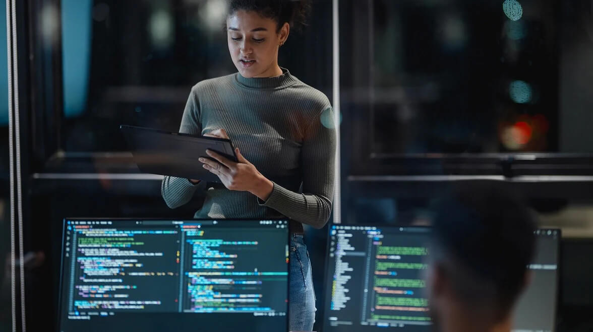 Cybersecurity professional analyzing code and system dashboards inside a secure operations room.