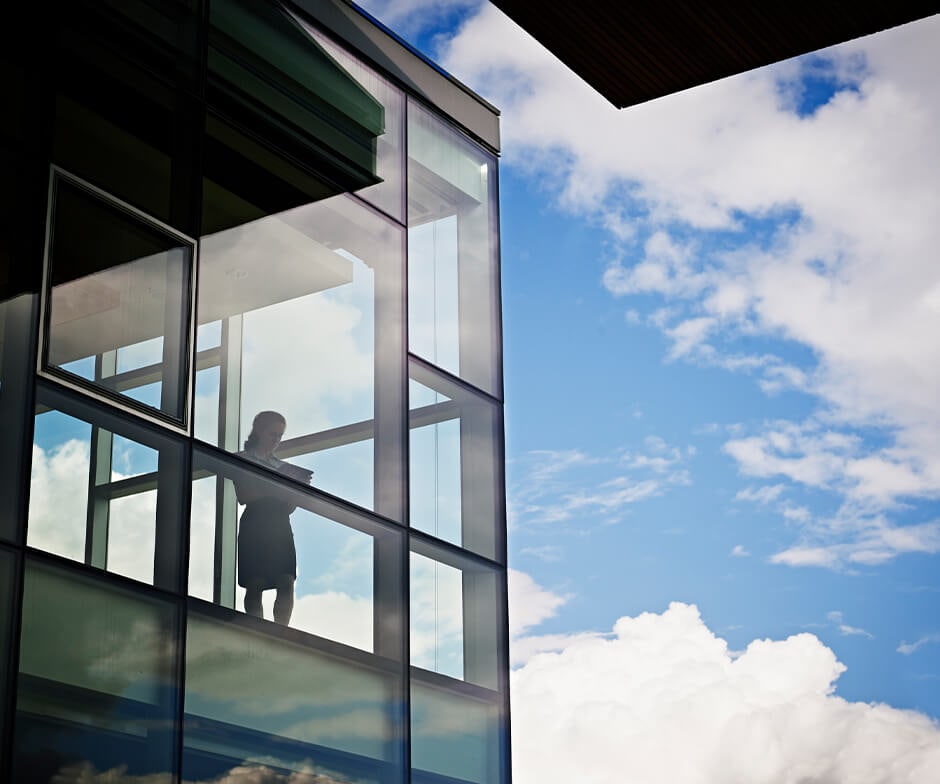 Woman looking out a building window into the sky.
