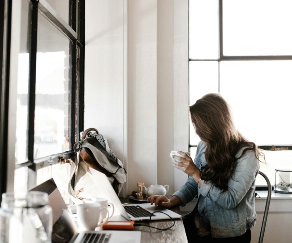 person sitting on chair and working on table while drinking coffee