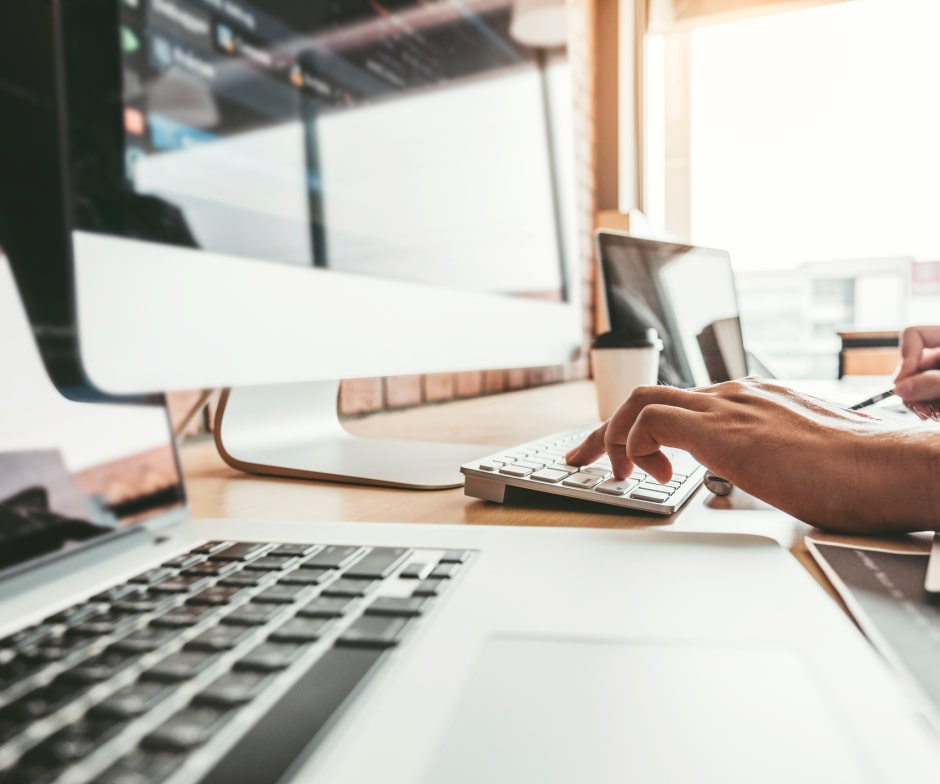 person typing on keyboard with in front of external monitor and coffee cup on table