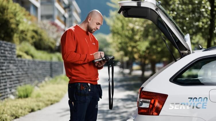 Man working on tablet behind a Service 7000 car with an open trunk