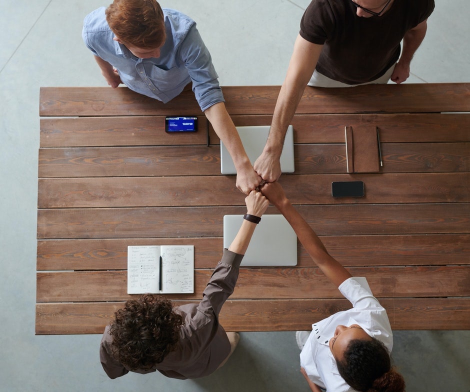 4 people with hands in a huddle over a workstation