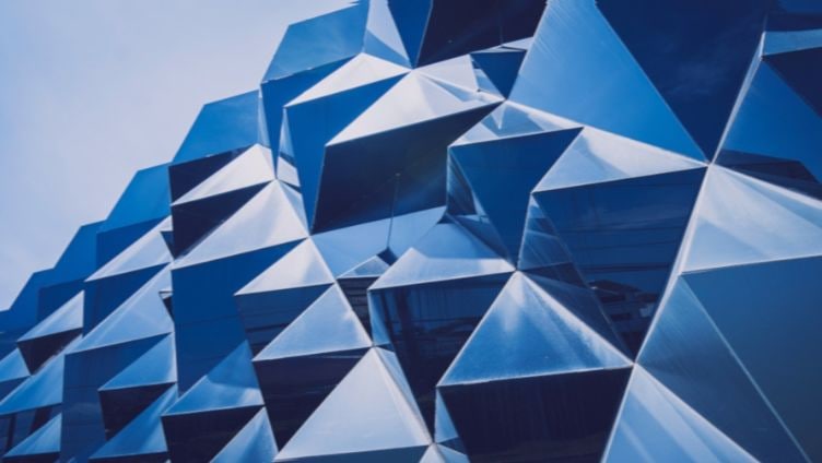 Gros plan sur la façade d'un bâtiment moderne présentant un motif géométrique de panneaux bleus angulaires et réfléchissants.