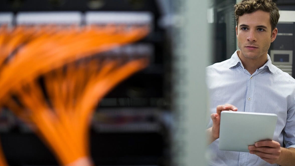 Engineer reviewing network infrastructure and orange cabling using a digital tablet.