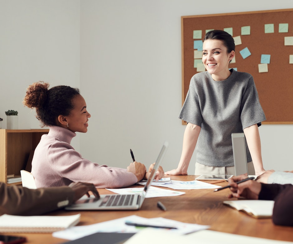 Woman standing at head of table, addressing a group of working people