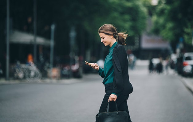 Frau, die beim Überqueren der Straße auf ihr Telefon schaut