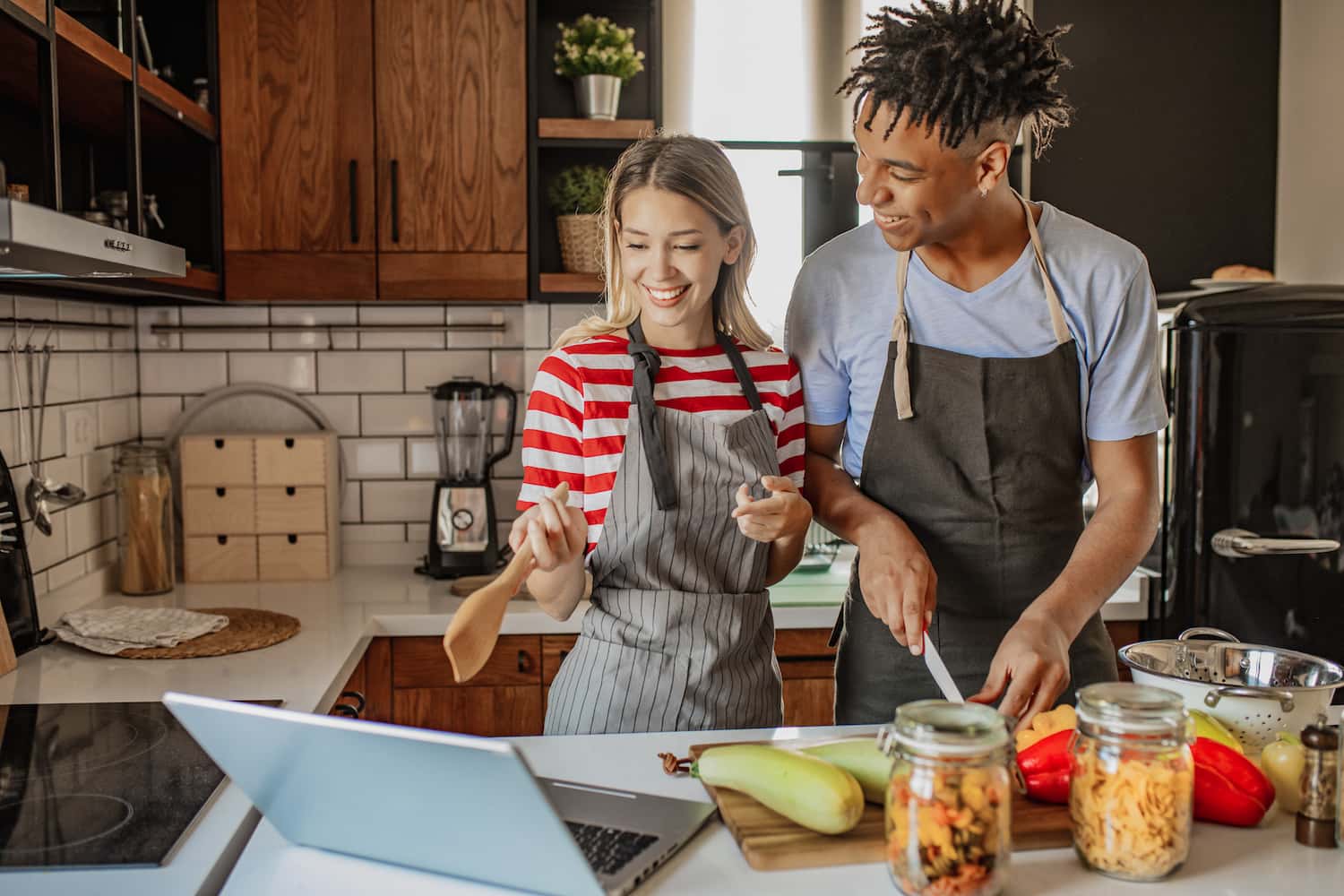 a man and women standing in a kitchen smiling preparing a meal from a recipe 