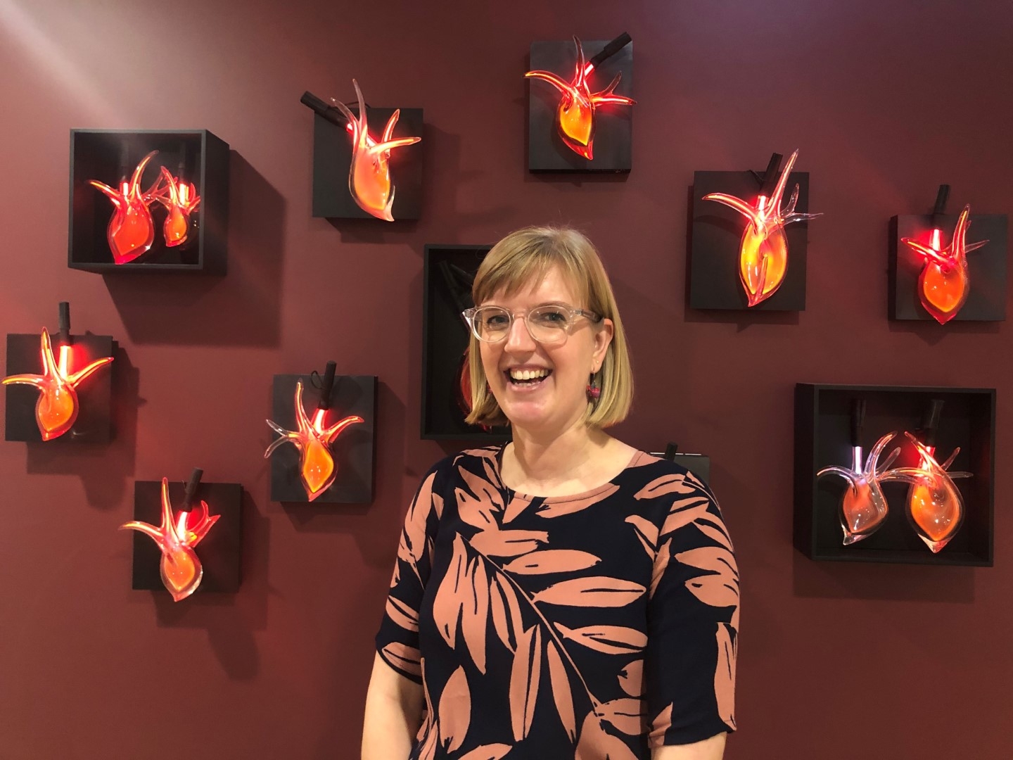 Dr Susie Cartledge smiling in front of a wall of beating hearts