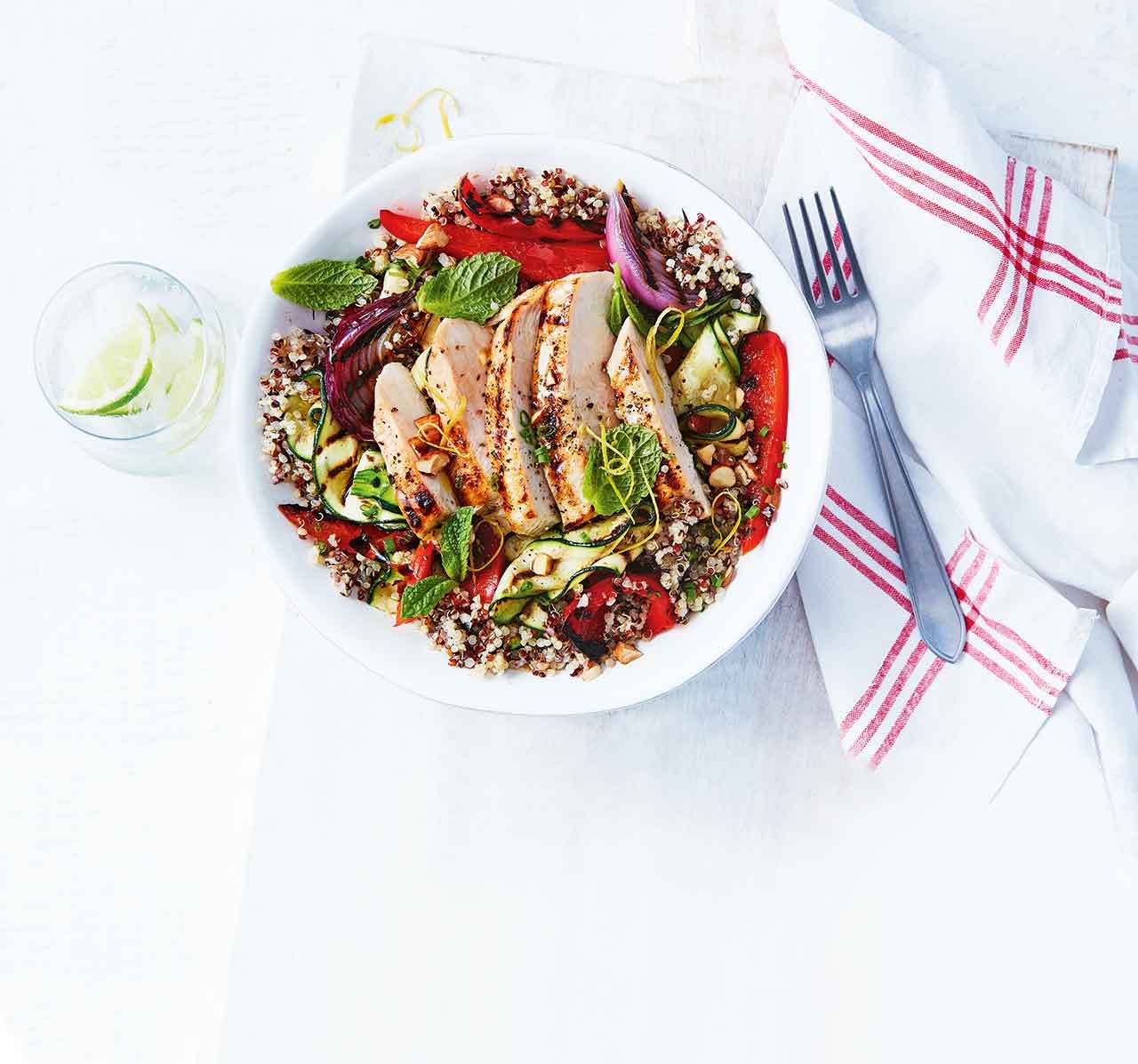 Plate of Chicken and zucchini quinoa salad with a glass of water, napkin and fork