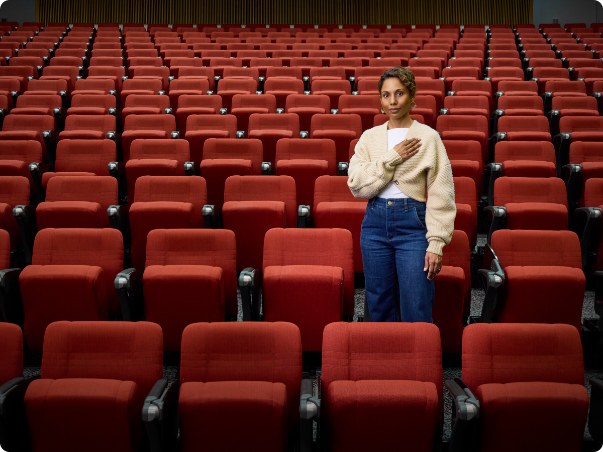 First Nations women (Dr Sonia Shah) standing in an empty lecture theater with her hand on heart 