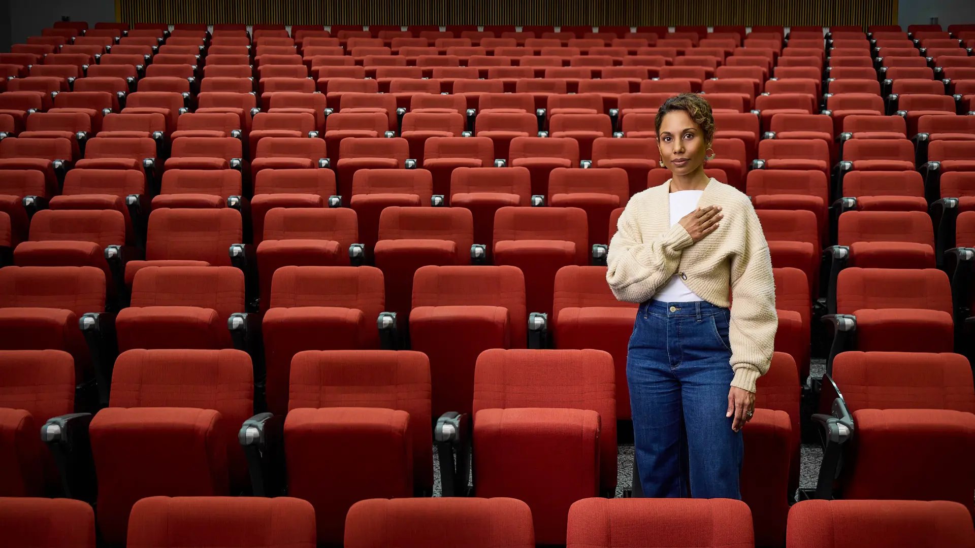 First Nations women (Dr Sonia Shah) standing in an empty lecture theater with her hand on heart 