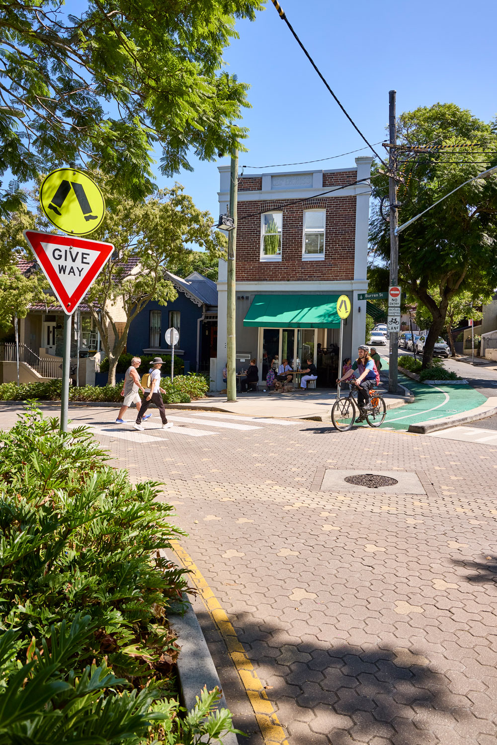 People walking and cycling through a neighbourhood street with a pedestrian crossing and separated bike lane.