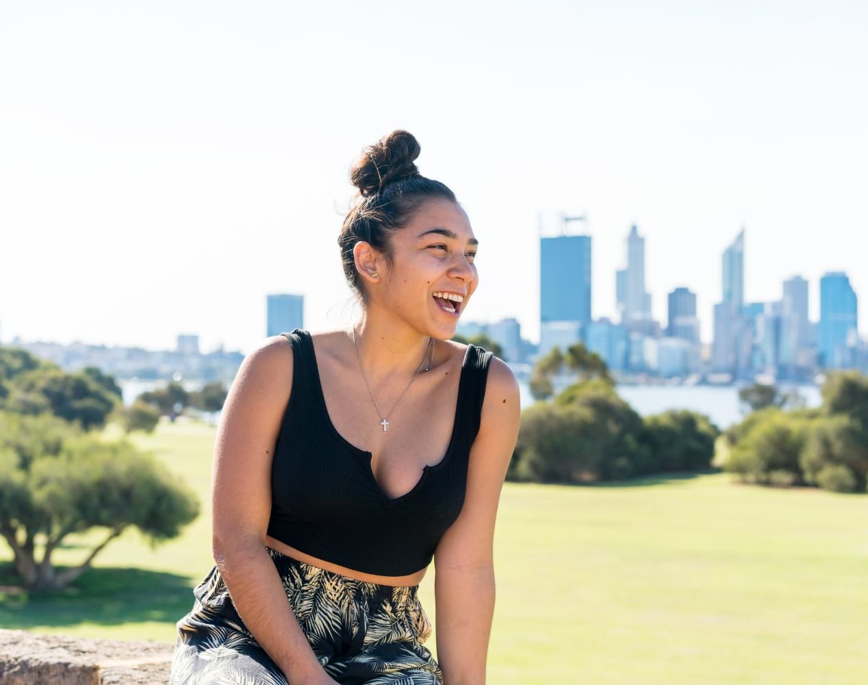 Person sitting outdoors on a grassy hill, with a blurred city skyline in the background.