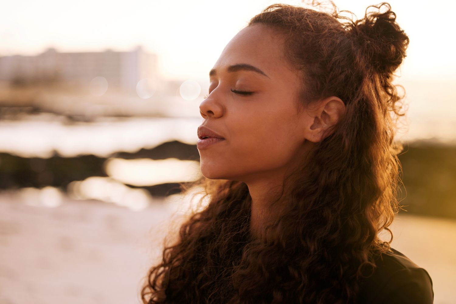 Shot of an attractive young woman sitting alone on a mat and meditating on the beach at sunset stock photo