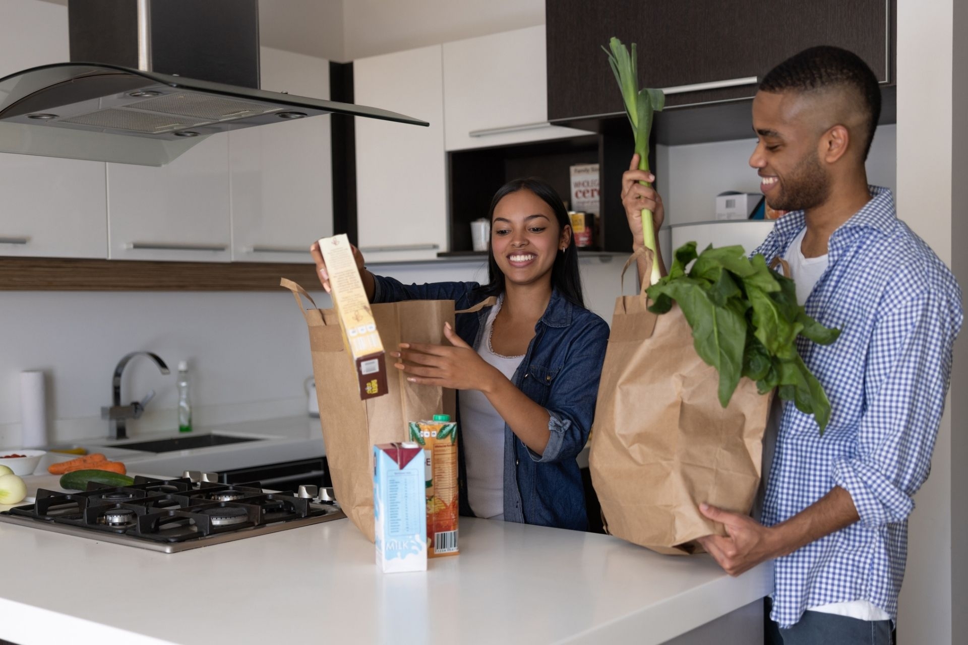 Happy couple of roommates unpacking the groceries at home after going shopping. 