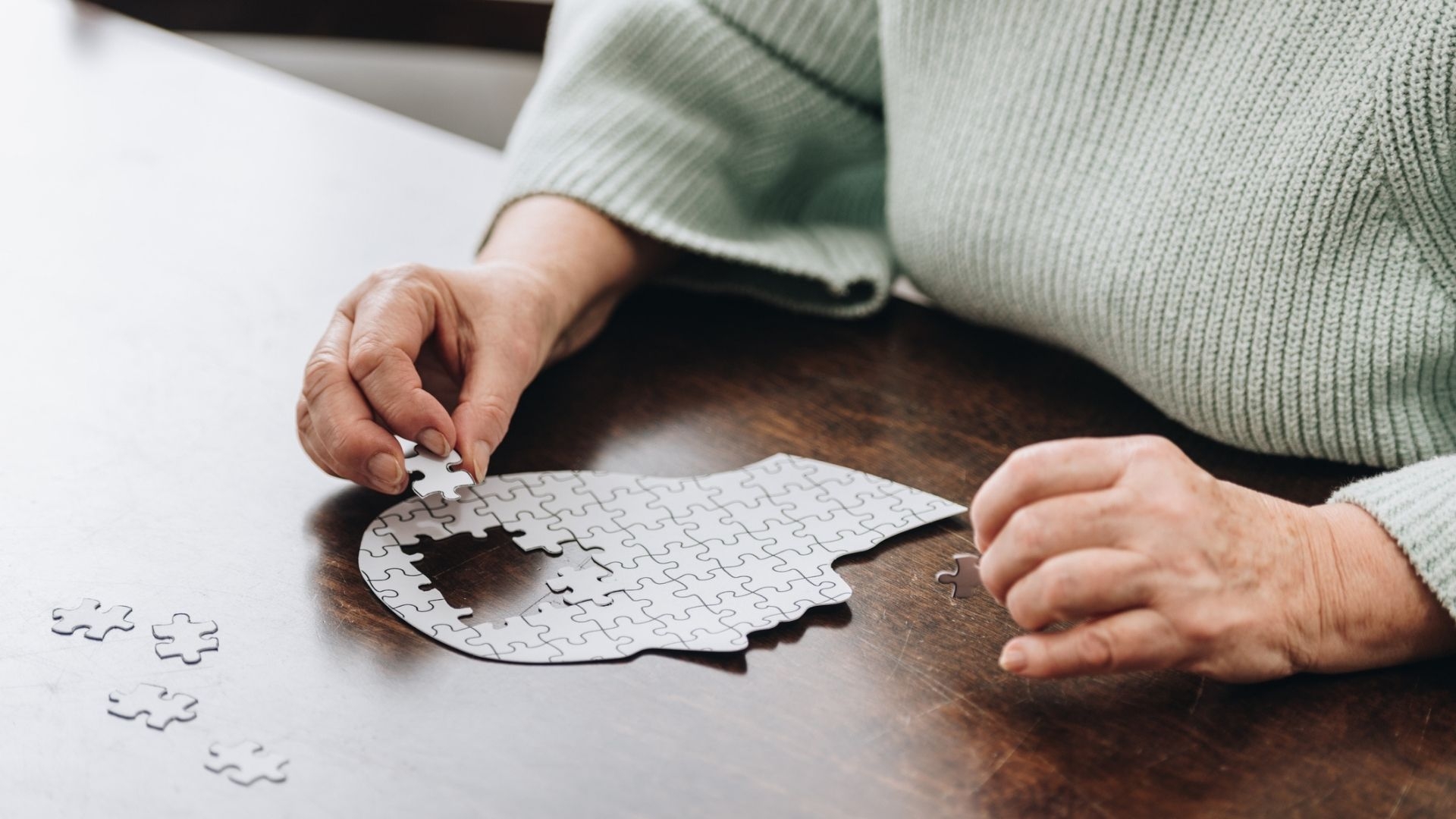 A cropped view of senior woman playing with a puzzle shaped like a human head