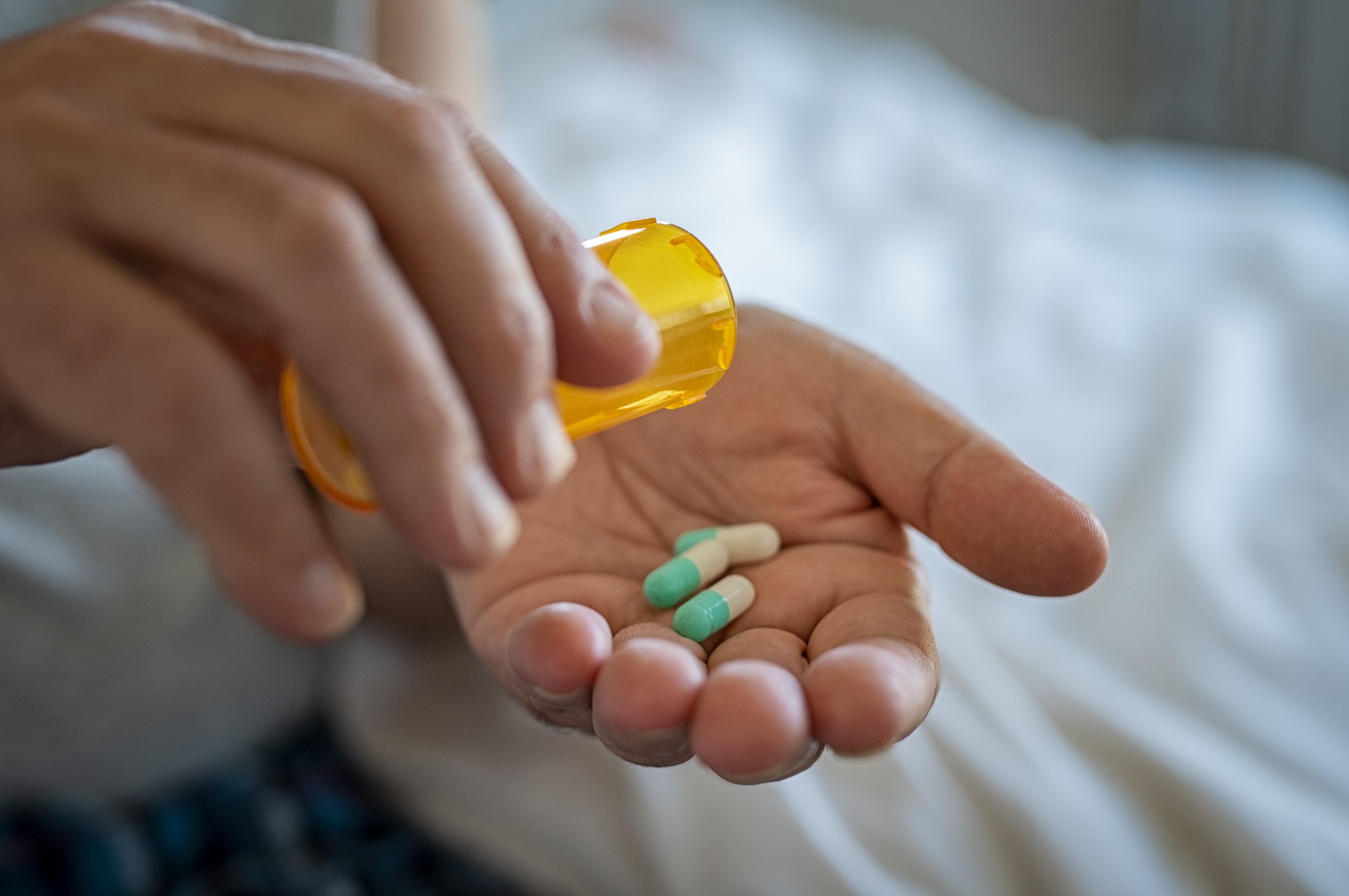 A person holding a pill bottle and a pill, indicating medication.