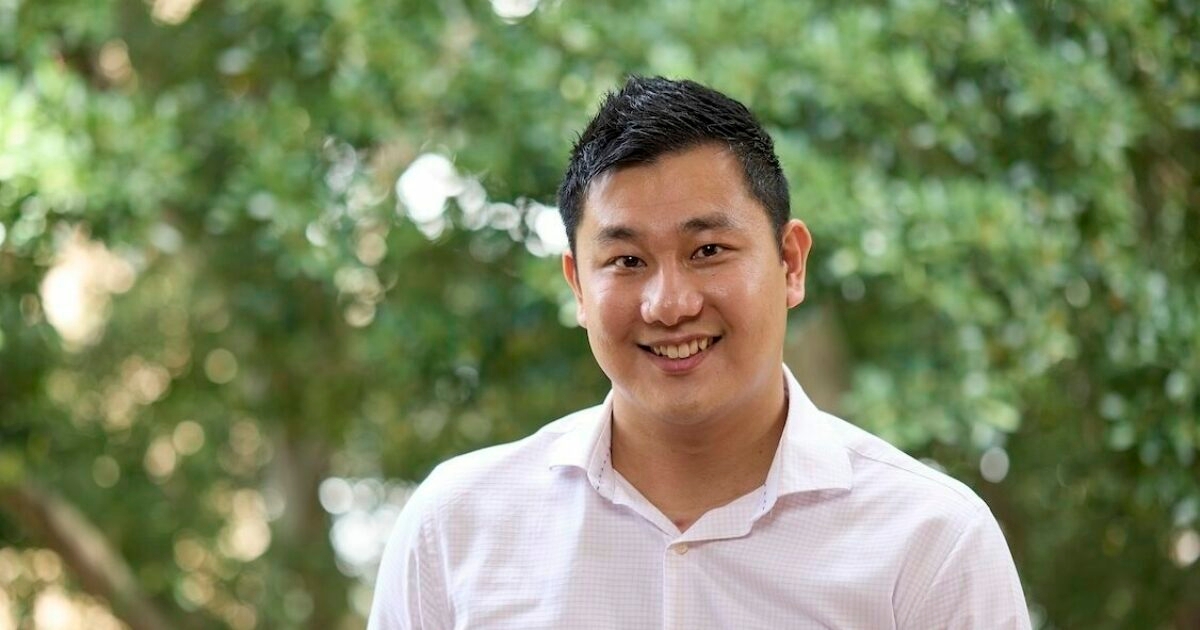 Derek Tran standing and smiling in a white shirt.