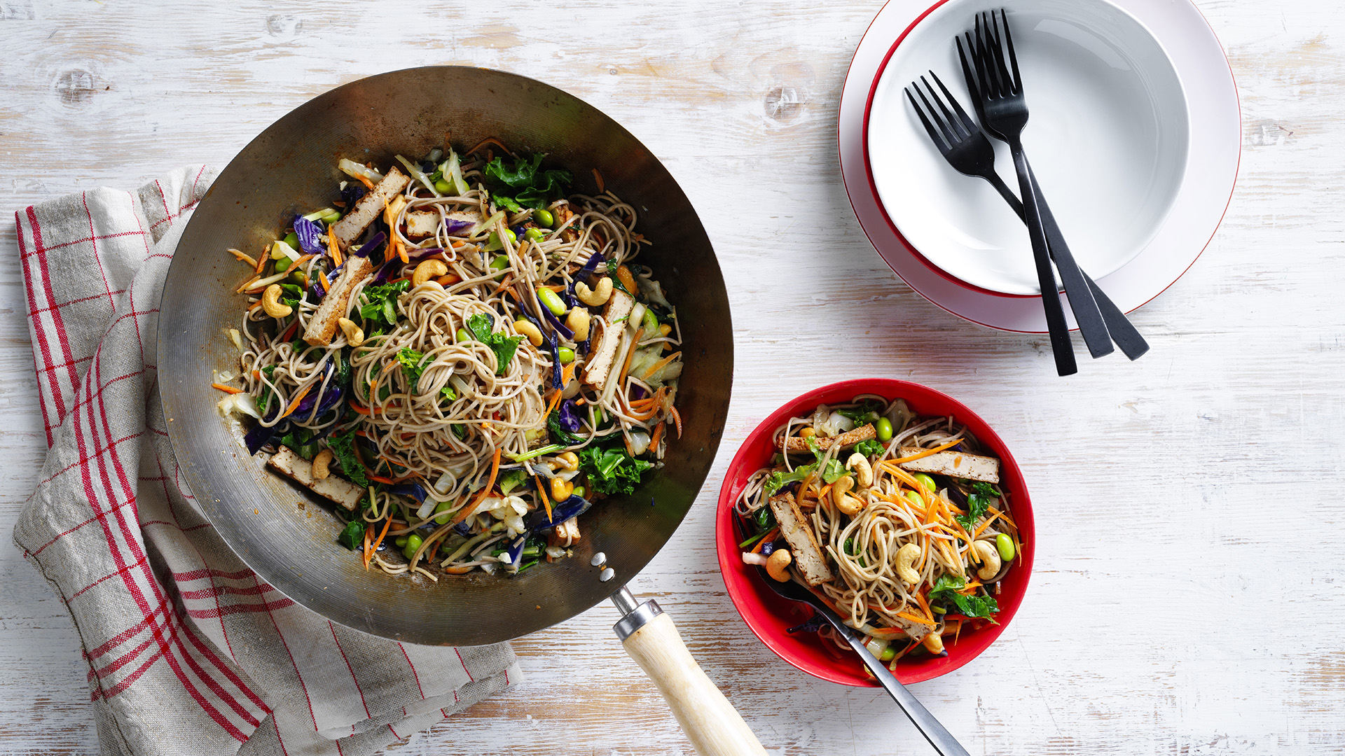 Honey soy tofu noodle stir-fry in a wok and a bowl on a table