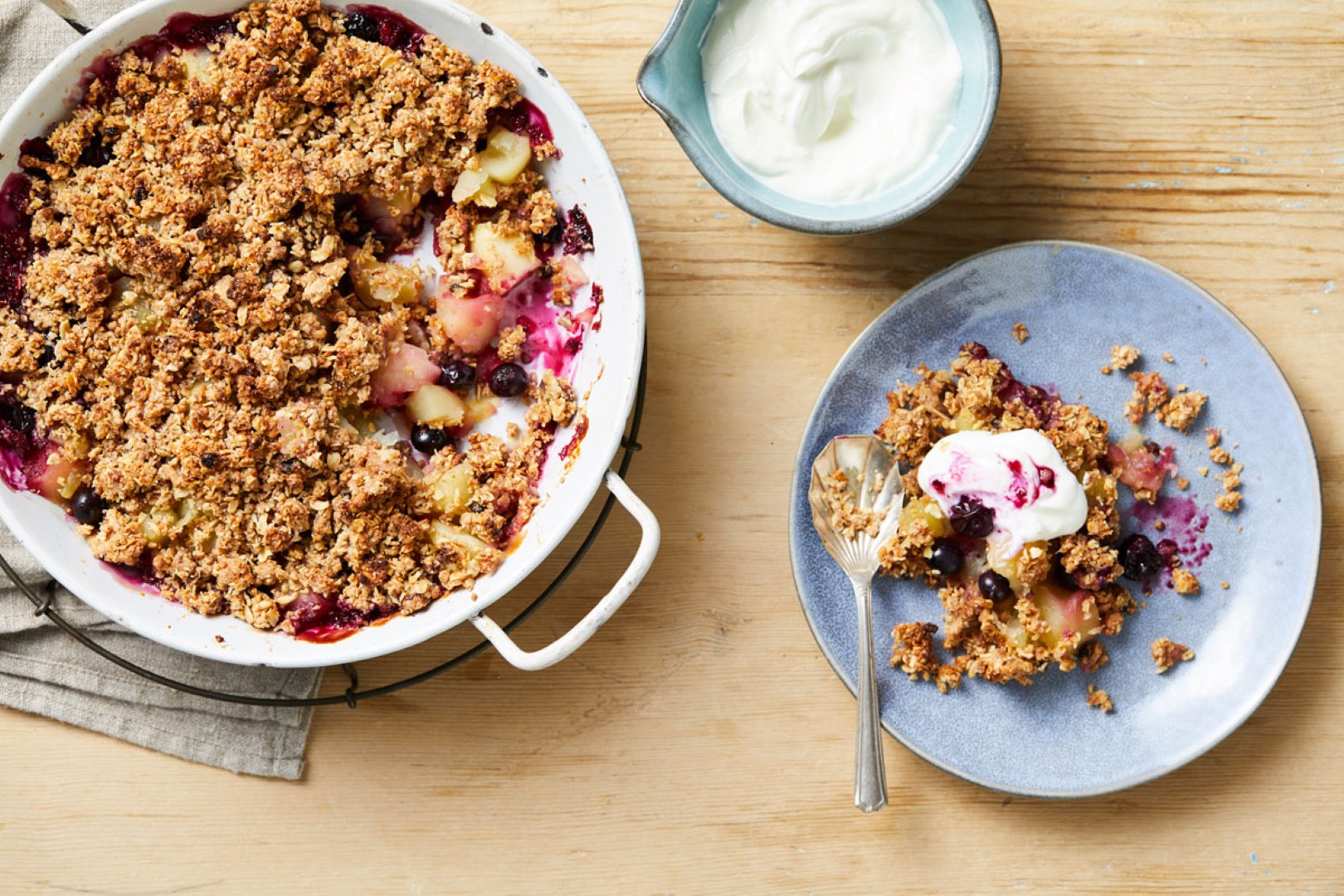 A bowl of yogurt accompanies a dish of fruit and crumble