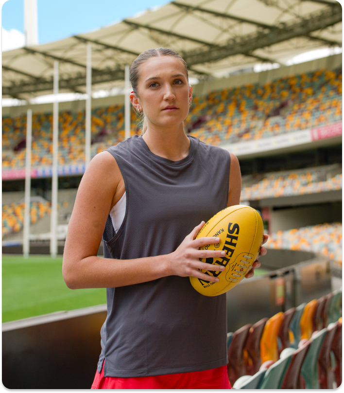 AFLW player Tay Smith holding a football standing in the stands in an empty stadium