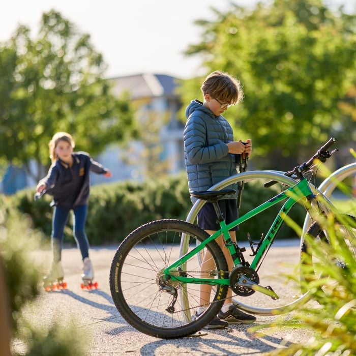 Child standing beside a bicycle while another child wears rollerblades on a shared pathway