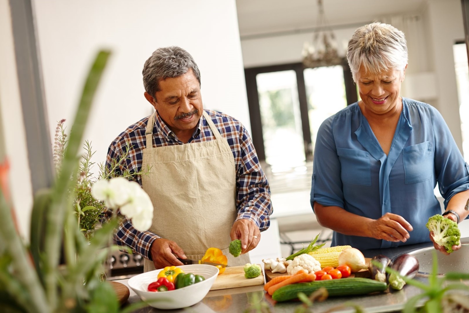 Older couple preparing fresh vegetables together in a bright kitchen, including broccoli, carrots, and peppers — making heart-healthy meals at home.