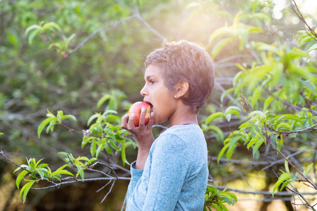 A young First Nations girl on a sunny day outdoors eating an apple