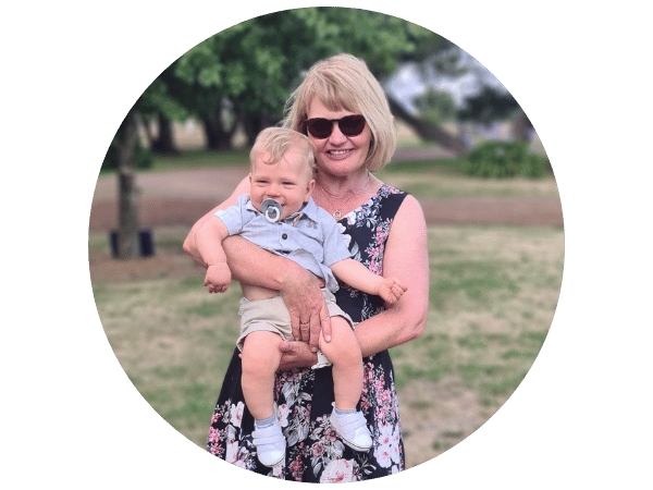 Sharon in a park, in sleeveless dress and sunnies, smiling, holding baby