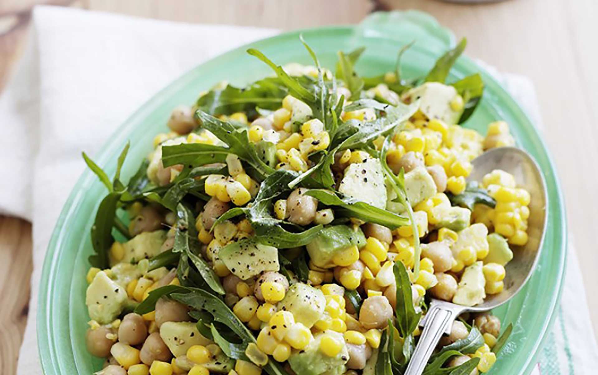 A bowl of corn salad featuring arugula and avocado