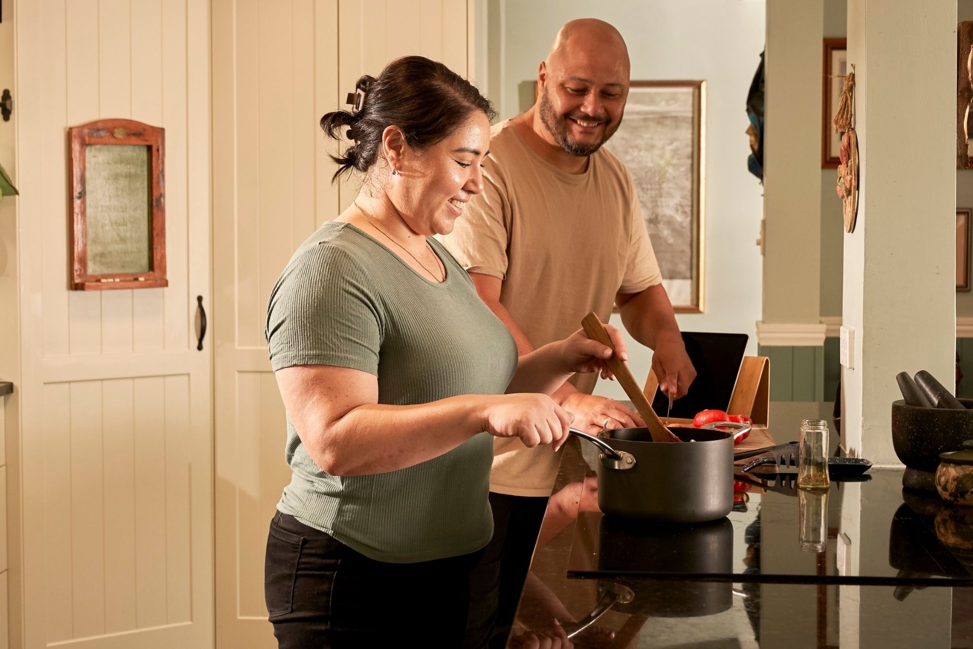 A couple in the kitchen, and the woman is cooking with a pot on the stovetop