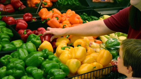 A woman choosing a red peppers from the fresh produce section.