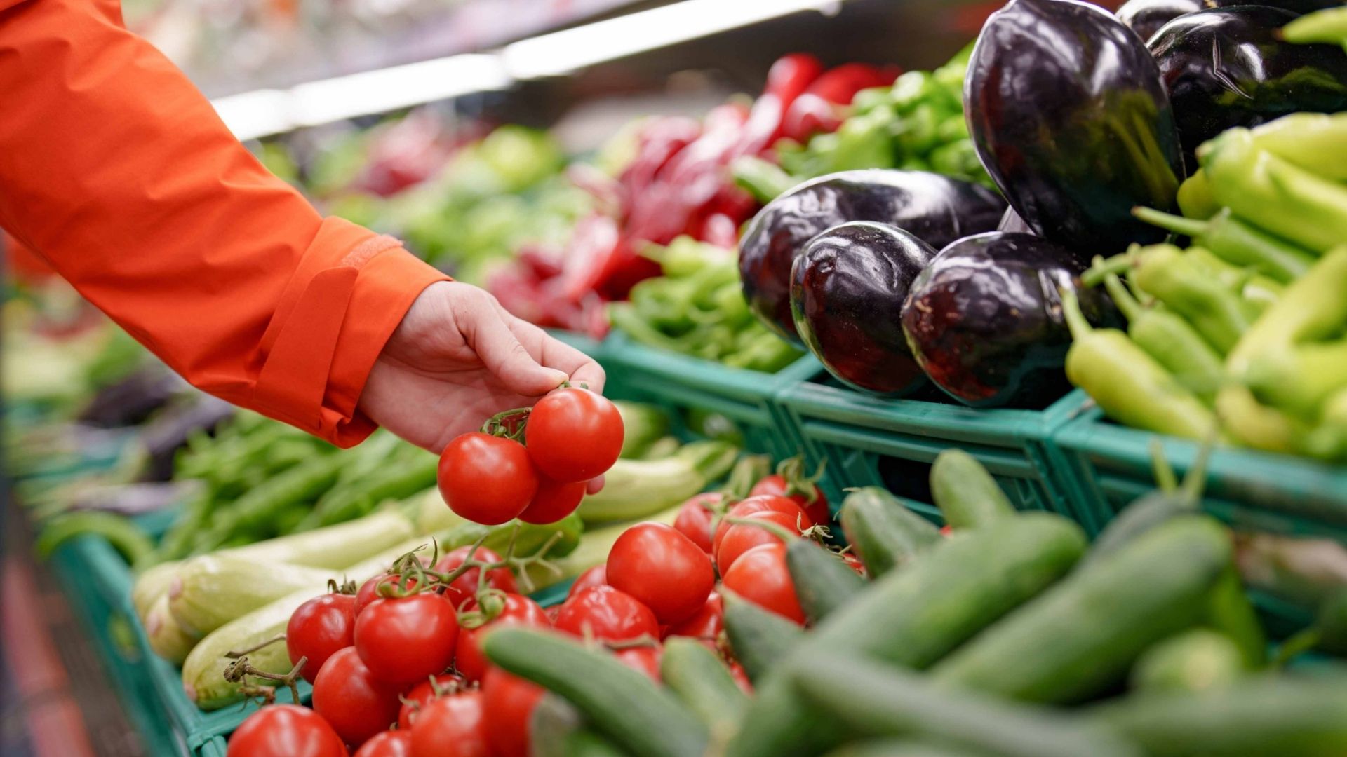 A person choosing a red tomatoes from the fresh produce section.