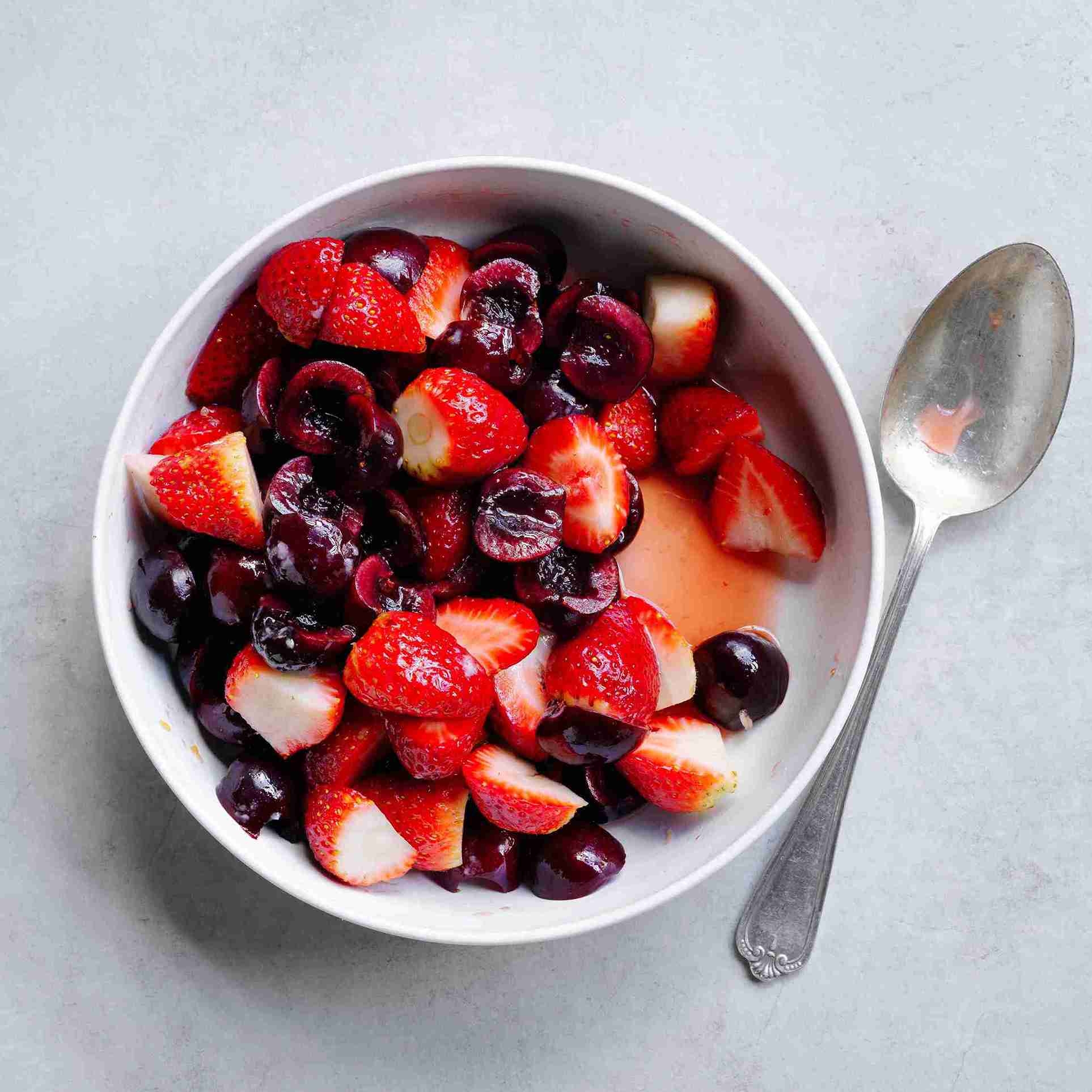 fresh fruit salad with cherries, strawberries, and orange juice tossed with icing sugar in a bowl