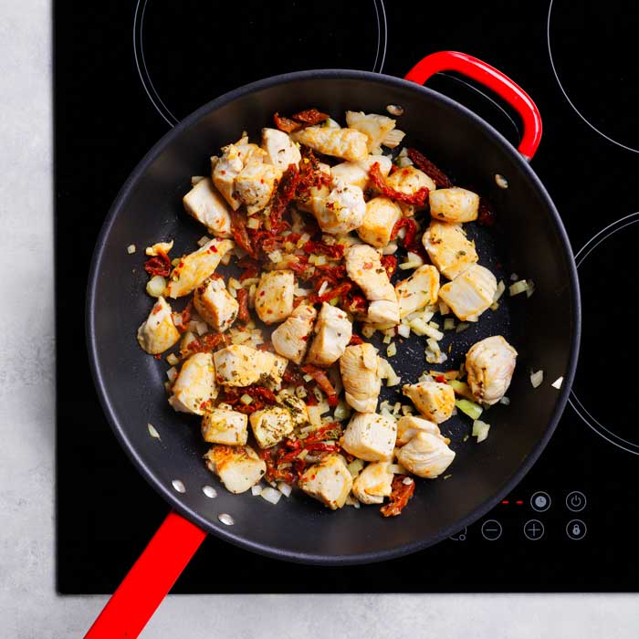 chicken pieces cooking in pan with sundried tomato, onion, garlic, herbs and chilli