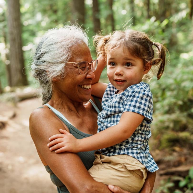 Smiling older woman holding a young girl, smiling, outdoors