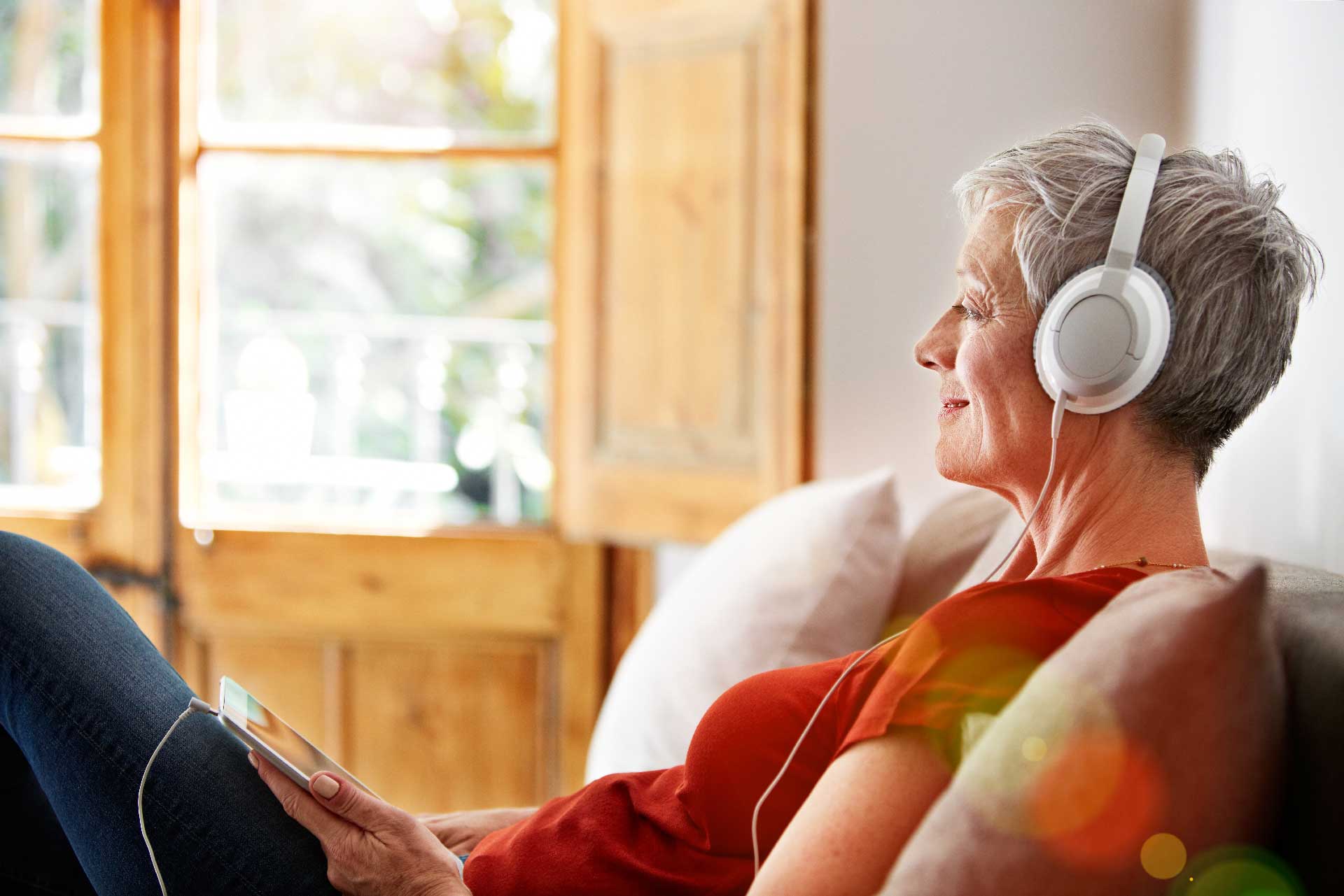 Mature woman with short grey hair smiling and listening to headphones, looking relaxed