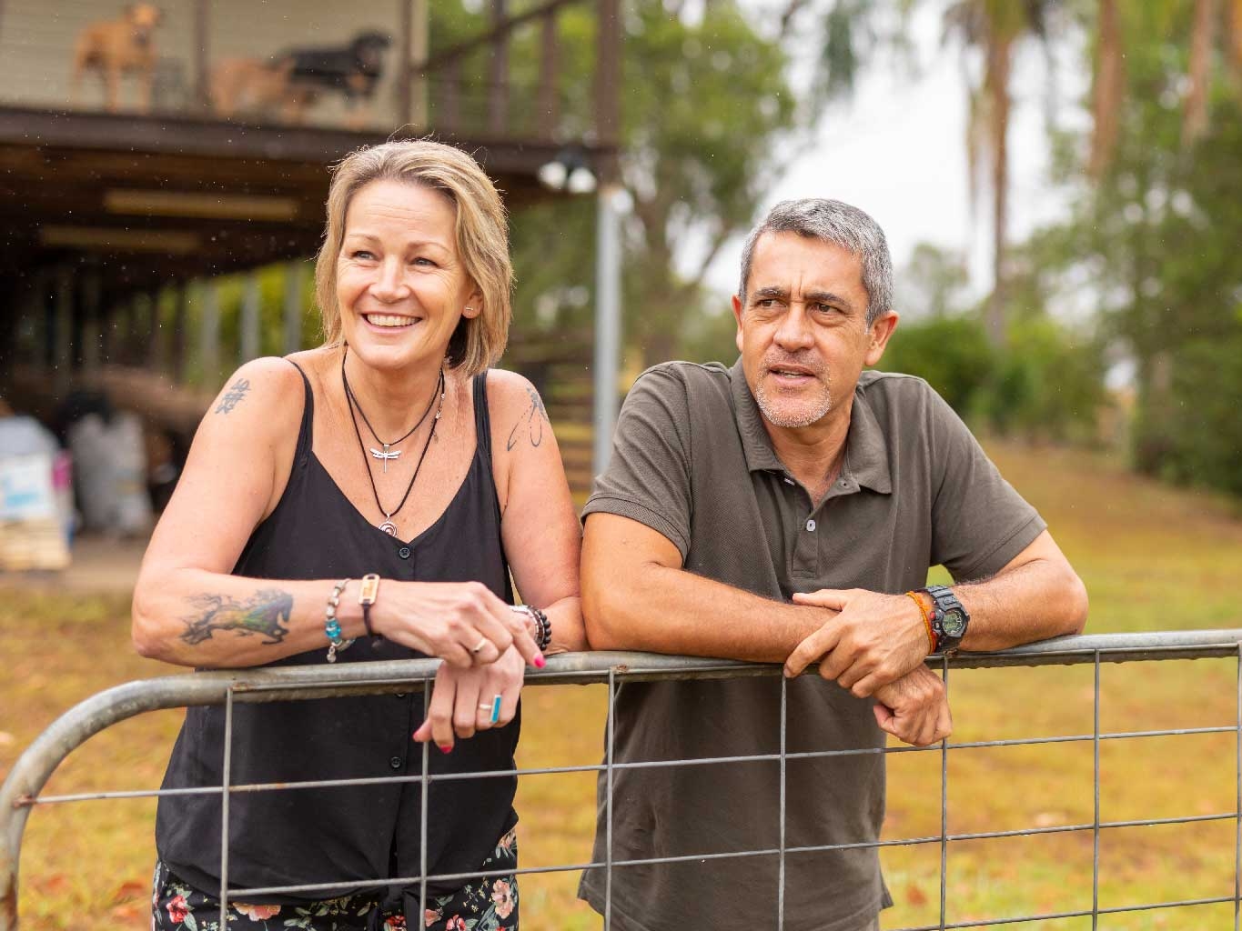 A man and woman standing behind a fence in front of a house.