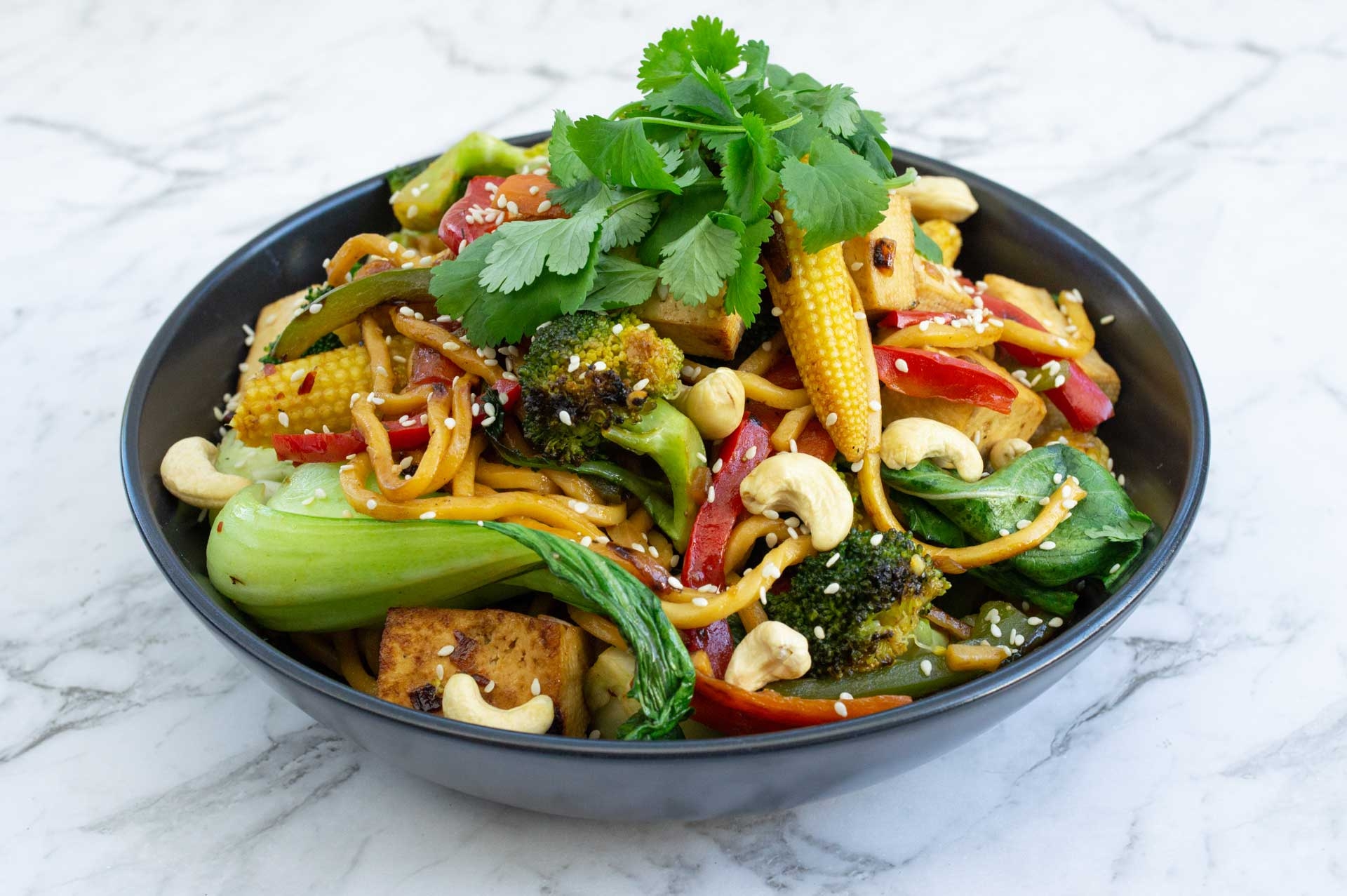 A delicious bowl of noodles topped with fresh vegetables, coriander and crunchy cashews.